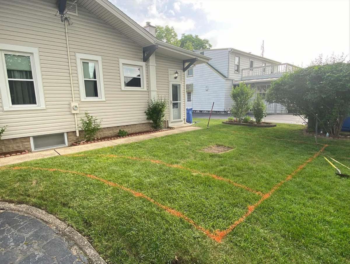 Backyard lawn marked with orange layout paint before paver patio installation