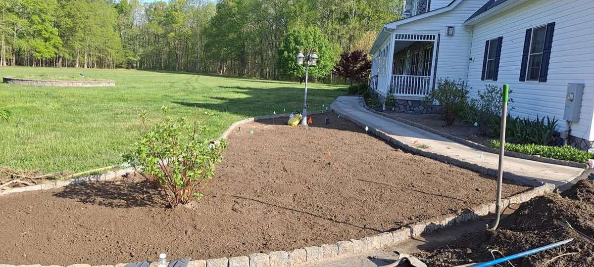 Planting bed stripped to bare soil with cobblestone edging before mulch