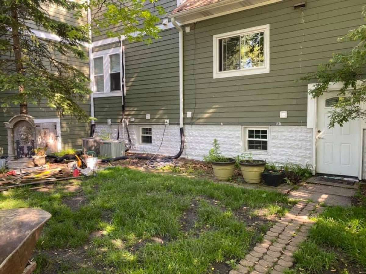 Weedy side yard with hoses and clutter along the foundation before work